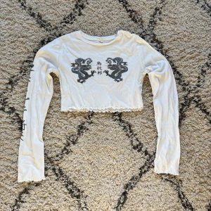 croppad långärmad topp - Vit långärmad croppad tröja med motiv på framsidan och ena ärmen!!