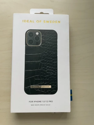 Svart croco mobilskal i guld från iDeal - Snyggt svart mobilskal med croco-mönster och gulddetalj från iDeal of Sweden. Passar iPhone 12/12 Pro. Skalet har en lyxig känsla och är gjort av djurvänligt material. Perfekt för dig som vill ha en trendig och stilren look.