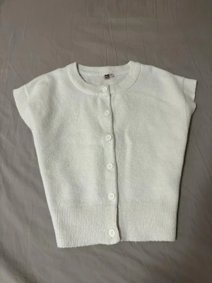 Vit kortärmad kofta med knappar - Vit knapp-topp från Nelly. Har använts och tvättats ett fåtal gånger men är i bra skick :)