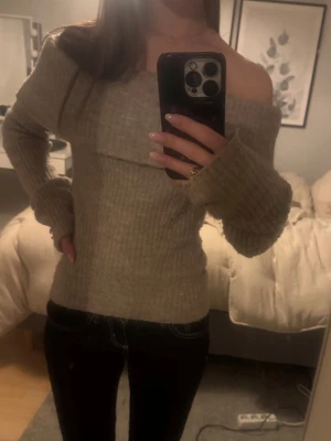 Beige off shoulder stickad tröja - Säljer en beige ribbstickad off shoulder-tröja med långa ärmar och bred krage. Tröjan har en mjuk och stretchig passform.