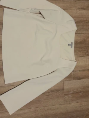 Vit långärmad topp med fyrkantig ringning - Stilren vit topp med lång ärm och snygg fyrkantig ringning. Perfekt att matcha med jeans eller kjol för en clean look. Tidlös design och mjukt material som känns skönt mot huden.