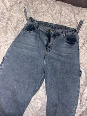 Baggy ljusblå jeans med fickor - Baggy jeans i ljusblå denim med flera fickor på sidorna och klassisk femficksdesign. Jeansen har bred passform och raka ben, perfekt för en avslappnad streetstil. Bälteshällor och knappgylf upptill.