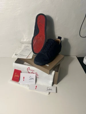 Mörkblå sneakers från Christian Louboutin - Snygga mörkblå sneakers från Christian Louboutin i mocka med den ikoniska röda sulan. Skorna har rund tå, snörning och diskreta detaljer. Perfekta för dig som vill ha något exklusivt och stilrent i garderoben.