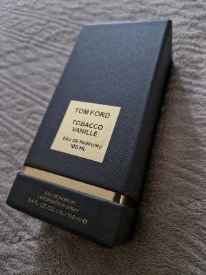 Tom Ford Tobacco Vanille 100 ml - Exklusiv parfym från Tom Ford, Tobacco Vanille, i en elegant svart och guld rektangulär flaska på 100 ml. Flaskan har en lyxig känsla med guldfärgade detaljer och tydlig märkning på framsidan. Eau de Parfum med en unik och djup doftprofil.