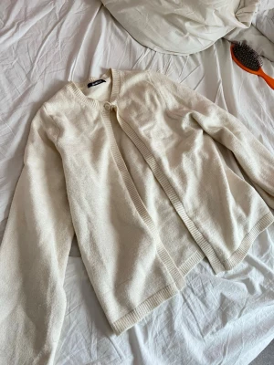 Krämvit kofta från Gina Tricot - Säljer en stickad kofta från Gina Tricot. Koftan har rund halsringning, ribbade muddar och knäpps med en knapp upptill. 