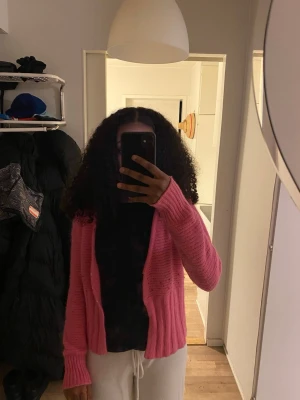 Rosa stickad kofta med pärldetaljer - Säljer en söt rosa stickad kofta med v-ringning och små pärldetaljer framtill. Koftan har långa ärmar och ribbstickad nederkant, perfekt att slänga över en t-shirt. Mjuk och skön, passar till många outfits!