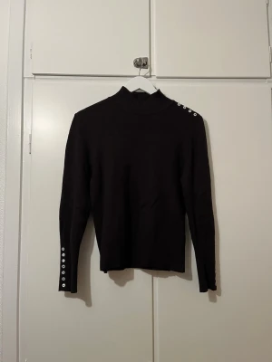 Brun tröja med knappar - Brun stilren, ish stickad tröja i stl S. (Jag brukar bära s/m och tycker den sitter bra) Tröjan har lite högre hals och knappar längs ena axeln och vid ärmsluten. Den är knappt använd och i väldigt fint skick!🤎