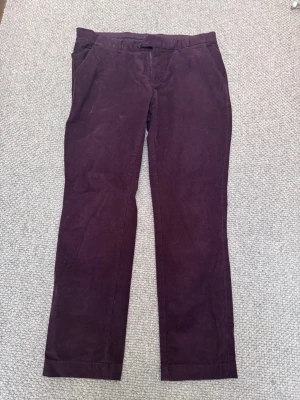 Vinröda manchesterbyxor raka ben - Säljer ett par vinröda manchesterbyxor med raka ben och klassisk passform. Byxorna har bälteshällor, snedställda fickor fram och stängs med knapp och dragkedja. Perfekta för dig som gillar retrostil och mjukt material.