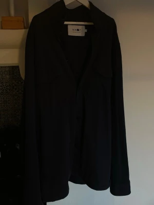 Svart overshirt från NN07 - Stilren svart overshirt från NN07. Perfekt lager på lager-plagg i mjukt tyg som passar till många olika stilar. Passar perfekt till vår, höst och sena sommarkvällar!