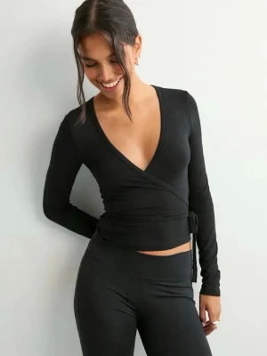 Populär svart omlottopp från Nelly. - Svart långärmad omlottopp från Nelly med knyt i sidan och djup v-ringning. Tunn och mjuk i materialet, liten i storlek. Sparsamt använd, nyskick.