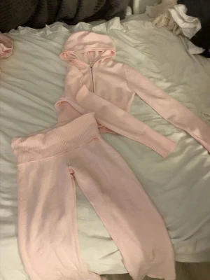 Ljusrosa mjukis-set med hoodie - Supermysigt loungewear-set i ljusrosa med croppad hoodie och dragkedja framtill samt matchande byxor med bred ribbad midja. Perfekt för chill dagar hemma. Materialet är mjukt och stretchigt stickat tyg.