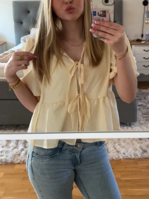 Ljusgul blus med knyt fram - Supersöt ljusgul blus med korta ärmar och knyt framtill. Köpt second hand och lappen är bort klippt så vet tyvärr ej märke 