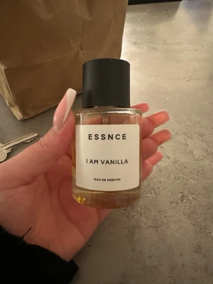 ESSNCE I Am Vanilla Eau de Parfum - En stilren parfym från ESSNCE med doften I Am Vanilla. Flaskan är cylindrisk i genomskinligt glas med svart matt kork och enkel vit etikett. Innehållet är gyllengult och flaskan har en modern, minimalistisk design som känns lyxig och trendig. Lite använd därav pris 