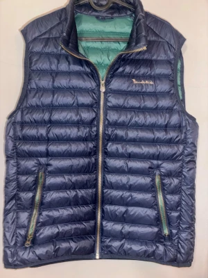 Mörkblå dunväst från Bondelid  - Snygg mörkblå dunväst från Bondelid med quiltad design och dragkedja framtill. Västen har två fickor med dragkedja och en grön insida som ger en cool kontrast. Perfekt för lager-på-lager och håller dig varm under kyliga dagar.