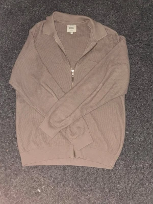 Beige stickad ziptröja från REBEL - Säljer en beige stickad ziptröja från REBEL med krage och bröstficka. Tröjan har långa ärmar, ribbade muddar och en snygg, enkel design som passar till det mesta. Perfekt för lager på lager och chill stil. Änvänd 1 gång, bara höra av dig vid frågor!