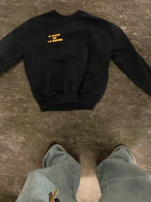 Svart sweatshirt med gul text - Cool svart sweatshirt med trycket 'D'ONCE DE LA SENSE' i gult på bröstet. Tröjan har rund hals, ribbade muddar och avslappnad passform. Perfekt för en chill och stilren look.