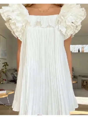 Vit plisserad klänning med volang - Supersöt vit kortklänning med plisserad kjol och stora volangdetaljer vid axlarna. perfekt för sommarens alla tillfällen eller student!!! 
