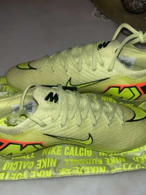 Nike Mercurial fotbollsskor gul/neon - Säljer ett par Nike Mercurial fotbollsskor elites  i ljusgul och neonfärg med svarta detaljer och stora Mercurial-loggor på sidan. Skorna har snörning, låg profil och är tillverkade i ett lätt syntetmaterial för bästa grepp på planen. Priset kan diskuteras. 