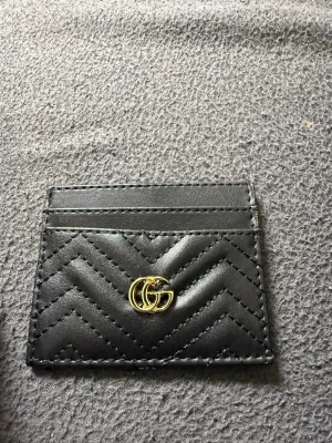 Svart kortfodral från Gucci - Snyggt svart kortfodral från Gucci i läder med quiltat mönster och guldfärgad GG-logga framtill. Fodralet har flera kortfack och en stilren design som känns både lyxig och modern. Perfekt för dig som vill ha koll på korten med stil.