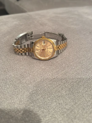 Seiko (mod)  - Säljer en Seiko mod Datejust med tvåtonad länk. Klockan har en rund urtavla i guldfärg med datumfönster och räfflad bezel. Länken är i rostfritt stål, vilket ger en tidlös och lyxig känsla. Perfekt accessoar för dig som gillar exklusiv stil. Lite små skavanker på klockan men inget som syns mycket. 