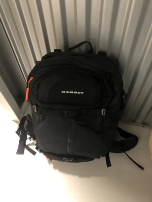 Svart skidryggsäck från Mammut - Snygg svart ryggsäck från Mammut med flera fack. Väskan har justerbara axelband, midjebälte. Perfekt för dig som vill ha en praktisk och stilren ryggsäck i slitstarkt material till din säsong i Alperna. Nypris: 2000 kr