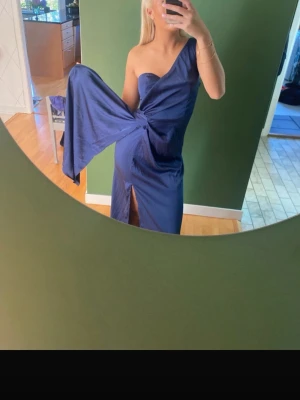 Marinblå balklänning/ brudklänning  - Säljer en marinblå långklänning i oneshoulder-modell med snygg drapering och knyt i midjan. Klänningen har en slits framtill och elegant asymmetrisk skärning. Perfekt för dig som vill sticka ut med en unik och trendig look.