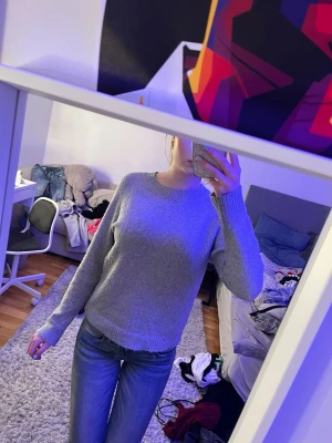 Grå basic stickad tröja - Enkel och stilren grå stickad tröja med rund halsringning och ribbade muddar vid ärmslut och nederkant. Perfekt att matcha med jeans för en avslappnad look. Materialet är mjukt och bekvämt.