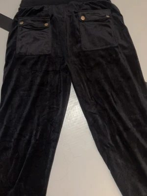Svarta byxor från Juicy Couture - Mysiga svarta  byxor från Juicy Couture. Byxorna har två fickor bak med knappar och en liten broderad logga framtill. Perfekta för en chill och trendig look. Jag har max använt dom 2 gånger och de är i storlek 15/16 (170) som passar S ungefär. Säljer pågrund av att de inte kommer till användning! 💕