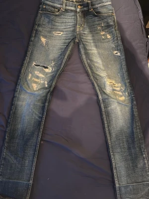 Blå slitna jeans från 7 for all mankind - Säljer ett par blå slim fit jeans från 7 for all mankind med slitningar och hål på både fram- och baksida. Jeansen har klassisk femficksmodell och är tillverkade i denim med snygg tvättad look. Perfekta för en avslappnad och trendig stil.