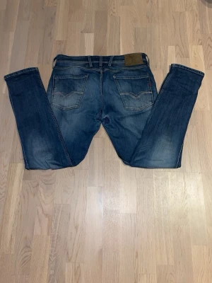 Replay Anbass - Säljer ett par klassiska blå Replay anbass jeans, passform slim och raka ben. Jeansen har fem fickor, perfekta till vardagslooken och tillverkade i slitstarkt denimtyg. Det finns en slitning i skrevet därför priset