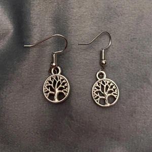Örhängen livets träd silver imitation  - Fina örhängen i form av livets träd. Berlockerna är ca 1 cm i diameter och gjorda av plast, men ser ut som metall.