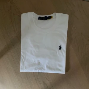 Vit t-shirt från Polo Ralph Lauren - Klassisk vit t-shirt från Polo Ralph Lauren med broderad marinblå logga på bröstet. T-shirten har rund halsringning och korta ärmar. Tillverkad i mjuk bomull för en skön och stilren look.