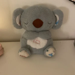 Nattlampa Koala Gosedjur - Mysig koala-nattlampa i mjuk plysch med inbyggd belysning i magen. Perfekt som nattlampa för barn. Lampan lyser med ett varmt sken. Gosedjuret är i gott skick, inga synliga defekter eller slitage. Batteridriven och enkel att använda.