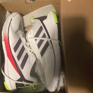 Adidas Novaflight 2 M sneakers vit/röd - Adidas Novaflight 2 M sneakers i vitt med svarta ränder, röda och neongula detaljer. Använda en gång. Rekommenderas till innebandy men funkar till vilken annan sport som helst. Strlk 44.