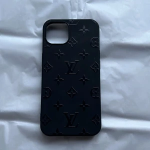 Louis Vuitton iPhone Skal (vet ej om äkta) - iPhone 13 Elegant svart Louis Vuitton-skal till iPhone med klassiskt LV-mönster. Skalet är i gott skick utan synliga repor eller skador. Ger din iPhone ett exklusivt och stilrent utseende samtidigt som det skyddar mot stötar och repor. Vet inte om den är ÄKTA 