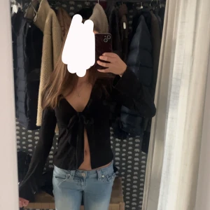 Svart omlottopp med knyt från Gina Tricot - Säljer en svart långärmad tröja med knyte framtill från Gina Tricot i storlek XS. Den är bara använd ett fåtal gånger så den är i mycket bra skick.💞