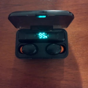 Trådlösa hörlurar med digital display och laddningsetui som även fungerar som powerbank  - Snygga trådlösa hörlurar med laddningsetui och digital batteriindikator som även fungerar som powerbank.Hörlurarna har orange detaljer och etuiet har både USB och micro-USB-port. Skick: bra, inga synliga defekter eller större slitage. Perfekt för musik och samtal på språng.