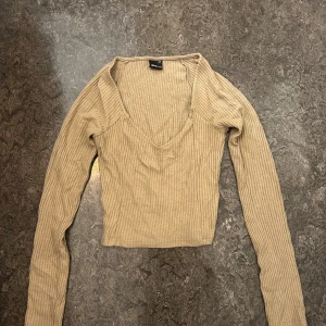 Beige Ginatricot långärmad topp - Säljer en beige ribbad långärmad topp från Gina Tricot i storlek XXS. Toppen har v-ringning och croppad passform, 