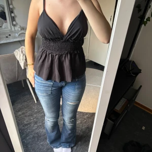 Svart linnetopp från Design by Si - Svart linnetopp från Design by Si med smala axelband, djup v-ringning och smockad midja som ger en snygg siluett. 