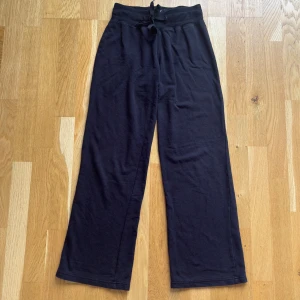 Svarta mjukisbyxor från Atmosphere - Svarta mjukisbyxor från Atmosphere med bred resår i midjan och snörning framtill. Byxorna har raka, lite vidare ben och är tillverkade i en mjuk bomullsblandning med polyester och elastan. Perfekta för chill dagar eller när du vill vara extra bekväm.