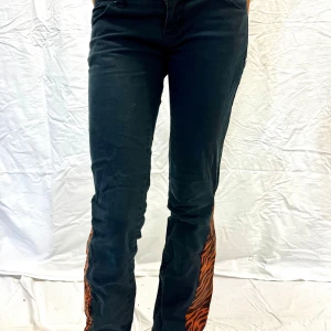 Lågmidjade jeans - Skitsnygga svarta Lågmidjade bootcut jeans med röd zebra detalj🦓 Perfekta utgångs jeans🤩🔥 Storlek 36   Innerbenslängd 80cm Midjemått 80cm  Pris kan diskuteras💗
