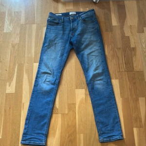 Blå slim straight jeans Jack & Jones - Snygga blå jeans från Jack & Jones i modellen Slim Straight Tim. Klassisk femficksdesign, orangea sömmar och normalhög midja. Jeansen är i stretchigt bomullsmaterial och har en rak men smal passform som sitter schysst på benen.