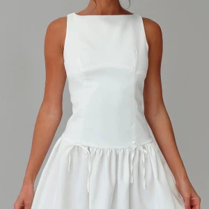 Vit kort klänning perfekt för studenten - Supersöt vit kort klänning med ärmlös design och rundad halsringning. Kjolen är voluminös och har två små knytband i midjan som ger en extra detalj. Perfekt för studenten, aldrig använd! säljer då för stor.