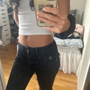 Mörkblå jeans lågmidjade - Snygga mörkblå jeans med låg midja och raka ben. Jeansen har råa, avklippta benslut och coola fickdetaljer med knappar både fram och bak. Klassisk femficksmodell i jeansmaterial, perfekta för en avslappnad stil.