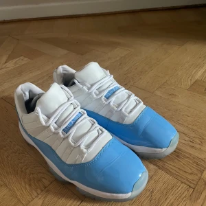 Nike Air Jordan 11 Low UNC blå/vit - Nike Air Jordan 11 Low UNC i fräscha blå och vita färger. Skorna har en glansig blå patentläderdetalj runt om, vit mesh och läder på ovandelen samt genomskinlig sula med blå detaljer undertill. Klassisk snörning och ikonisk siluett som sticker ut.