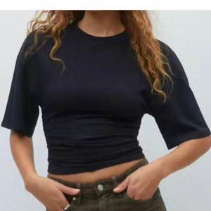 Svart croppad topp från Gina Tricot - Svart croppad topp från Gina Tricot med korta ärmar och rund halsringning. Toppen har snygg rynkdetalj i sidorna som ger en tight och figurnära passform. Perfekt till jeans eller kjol för en trendig look.