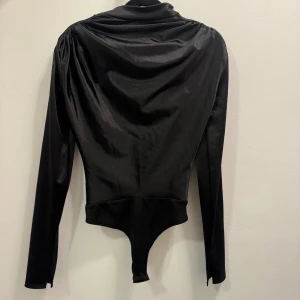 Svart långärmad bodysuit med drapering - En body från Nelly med slits vid handleden 