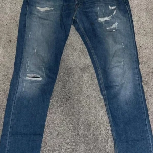 Replay jeans slim fit - Säljer ett par blå jeans med slim passform och slitna detaljer på både lår och knän. Jeansen har klassisk femficksdesign och är tillverkade i stretchigt denim för en bekväm känsla. Perfekta för dig som gillar en trendig och avslappnad look.