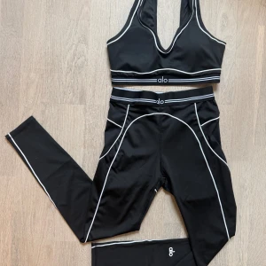 Alo Yoga träningsset - Säljer detta superpopulära träningsset från Alo Yoga, helt oanvänt och i perfekt skick! Setet består av topp och tights i lyxigt, stretchigt material som formar sig snyggt efter kroppen och ger en riktigt smickrande passform. De vita detaljerna ger en stilren kontrast mot det svarta. Perfekt både till gymmet och till vardags.❤️😍