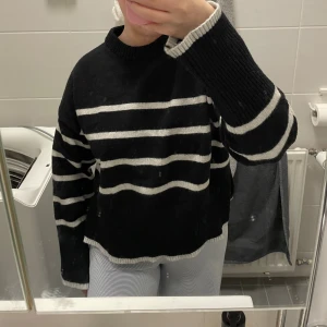 Svartvit randig stickad tröja - Svart stickad tröja från Bershka med vita horisontella ränder. Tröjan har en loose passform, rund halsringning och långa ärmar. Perfekt för lager-på-lager och chill vibes. Ribbstickade muddar vid ärmslut och nederkant.